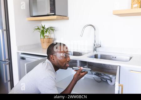 Der afroamerikanische Klempner repariert das Waschbecken während des Telefongesprächs Stockfoto