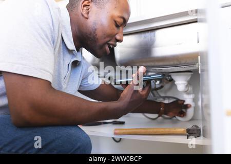 Der afroamerikanische Klempner repariert das Waschbecken während des Telefongesprächs Stockfoto