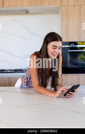 Eine junge weiße Brünette interagiert mit einem Smartphone in der Küche zu Hause Stockfoto