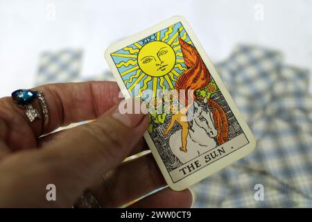 Hand einer Wahrsagerin, die eine Tarotkarte in der Hand hält. Es ist die Sonne. Diese Karte wird im Allgemeinen als positiv betrachtet. Es steht für Glück und Fortsetzung Stockfoto