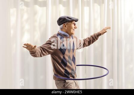 Fröhlicher älterer Mann, der Spaß hat und zu Hause einen Hula Hoop dreht Stockfoto