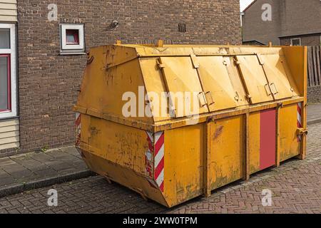 Ein gelber Industrieabfallbehälter aus Stahl mit geschlossenen Rollläden steht draußen auf einem Parkplatz in einem Wohngebiet Stockfoto