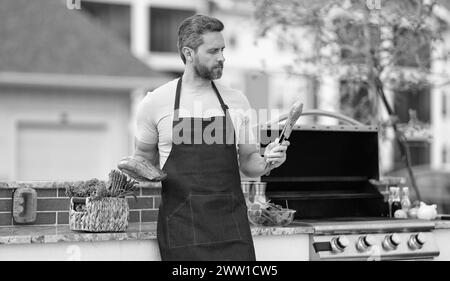 Koch mit gegrilltem Lachs. Küchenchef kocht gegrillten Lachs im Freien. Gegrillter Lachsfisch bei man trägt Küchenschürze. Foto des Küchenchefs mit gegrilltem Lachs. Stockfoto