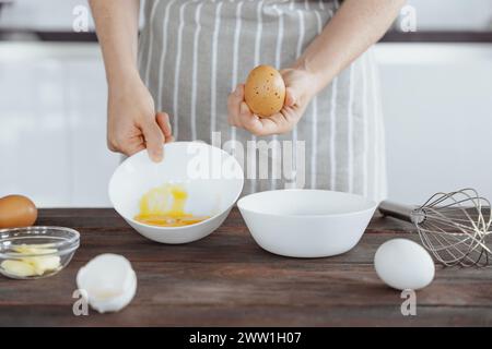 Frau in Schürze trennt Eiweiß von Eigelb in der Schüssel zum Rühren oder Backen, Hintergrund für die Küche, Zubereitung der Zutaten Stockfoto