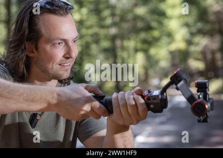 Content Creator verwendet. Ein Handy-Gimbal zum Filmen in der Natur mit einem verschwommenen Wald im Hintergrund Stockfoto