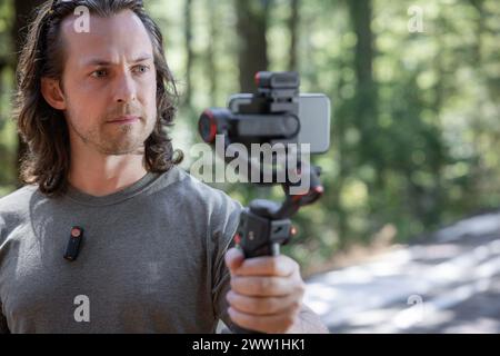 Content Creator verwendet. Ein Handy-Gimbal zum Filmen in der Natur mit einem verschwommenen Wald im Hintergrund Stockfoto