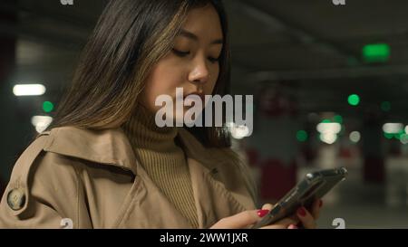 Ernsthafte asiatische Frau chinesisch koreanisch japanerin Mädchen ethnische Dame Kunde Fahrer in Tiefgarage Auto chatten Handy-Anwendung Stockfoto