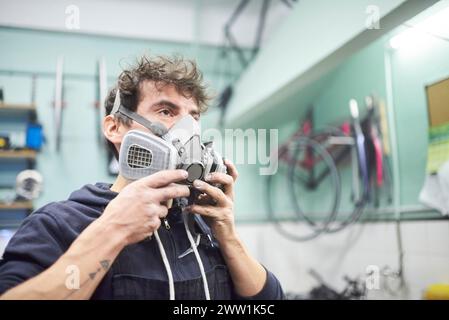 Porträt eines lateinischen jungen Arbeiters, der in seiner Werkstatt eine Atemschutzmaske aufsetzt. Echte Menschen bei der Arbeit. Stockfoto