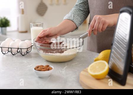 Frau macht Schokoladenteig mit Schneebesen in Schüssel an grauem Marmortisch, Nahaufnahme Stockfoto