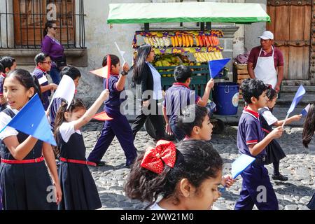 Antigua, Guatemala. März 2024. Schulkinder begleiten die Semana Santa Festival Queen, vorbei an einem Obstverkäufer, während sie durch das historische Zentrum zur Vorbereitung der heiligen Woche am 20. März 2024 in Antigua, Guatemala, marschieren. Die opulenten Prozessionen, detailgetreuen Alfombras und jahrhundertealten Traditionen ziehen mehr als 1 Million Menschen in die alte Hauptstadt. Quelle: Richard Ellis/Richard Ellis/Alamy Live News Stockfoto