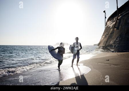 Ein Mann und eine Frau gehen am Strand und halten Surfbretter Stockfoto