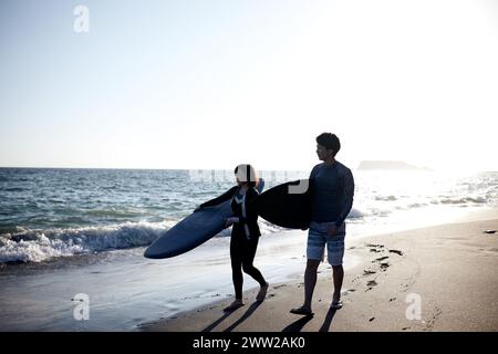 Ein Mann und eine Frau gehen am Strand und halten Surfbretter Stockfoto