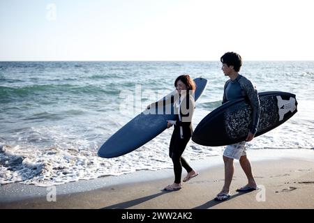 Ein Mann und eine Frau gehen am Strand und halten Surfbretter Stockfoto