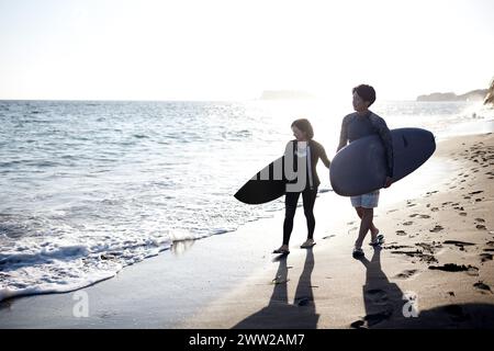 Ein Mann und eine Frau gehen am Strand und halten Surfbretter Stockfoto