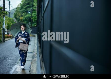 Eine Frau im Kimono, die eine Straße mit einem Regenschirm entlang läuft Stockfoto