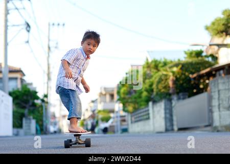 Ein kleiner Junge, der auf einem Skateboard die Straße runterfährt Stockfoto