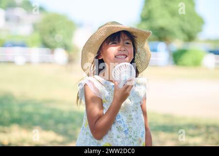 Ein junges Mädchen mit einem Hut, der einen weißen Ventilator hält Stockfoto