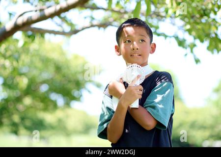 Ein kleiner Junge, der einen Ventilator in der Hand hält Stockfoto