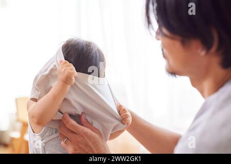 Asiatischer Vater hilft dem Kind, sich anzuziehen Stockfoto