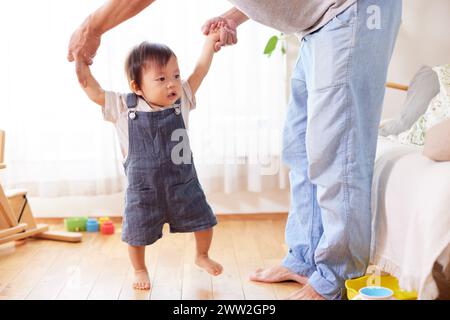 Ein Mann, der die Hand eines Kleinkindes hält, während er auf einem Holzboden steht Stockfoto