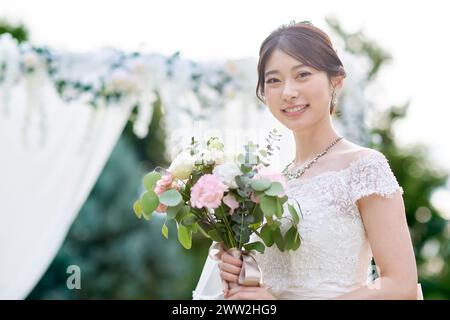 Asiatische Braut mit Blumenstrauß vor dem Hochzeitsbogen Stockfoto