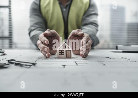 Architekt Ingenieur hält und schützt das Minihausmodell auf Bauplan. Protect House, Kostenplanung und Baukonzept. Stockfoto