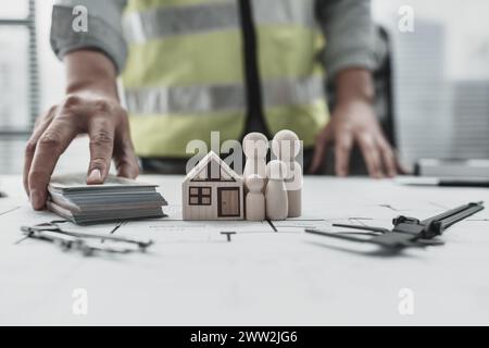 Hausmodell, Holzpuppe und Geld auf dem Hauslayout repersent Familie spart Geld beim Kauf eines Hauses. Architekt- und Ingenieurkonzept. Stockfoto