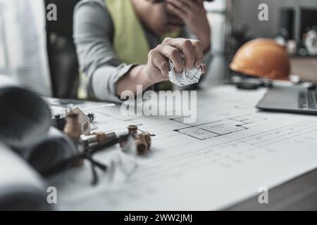 Der Architekt und Ingenieur machte einen Fehler beim Entwurf des Plans. Papier-Crump-Blueprint in der Hand. Fehler, Fehler und Problem Konzept. Stockfoto