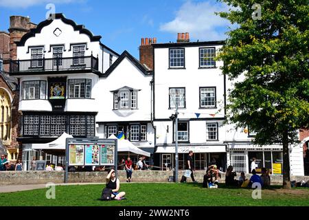 Vorderansicht der Mols und anderer Gebäude in der Kathedrale nahe Touristen, die die Sonne genießen, Exeter, Devon, Großbritannien, Europa. Stockfoto