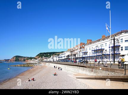Touristen entspannen sich am Strand und an der Promenade mit Hotels mit Blick auf das Meer, Sidmouth, Devon, Großbritannien, Europa. Stockfoto