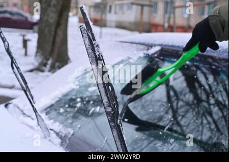 Schneeräumung von der Windschutzscheibe des Autos. Die Scheibenwischer des Fahrzeugs sind angehoben. Stockfoto