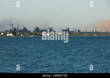 Industrielle Skyline mit metallurgischer Anlage über Wasser. Rauch, der in den Himmel ausgestoßen wird, symbolisiert Fabrikemissionen, Luftverschmutzung und Umwelt Stockfoto