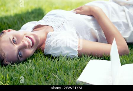 Schwangere, Frühling und Porträt einer Frau, die Buch in der Natur im Freien liest, für Entspannung, Wellness und Frieden auf dem Feld. Schwangerschaft, Literatur und Mutterlügen Stockfoto