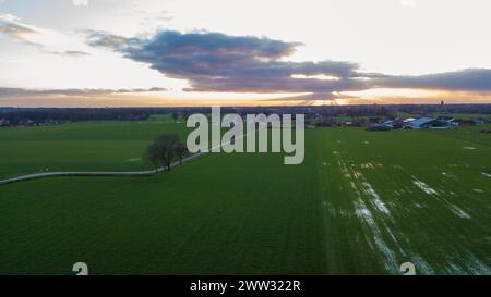 Der abendliche Himmel zieht sich durch eine ländliche Umgebung mit Sonnenstrahlen, die durch Wolken dringen und dramatische Schatten über die grünen Felder werfen. Diese Luftaufnahme fängt die ruhige Schönheit der Landschaft ein, wenn die Nacht näher rückt. Aus der Vogelperspektive der Sonnenstrahlen, die durch Wolken über der ländlichen Landschaft brechen. Hochwertige Fotos Stockfoto