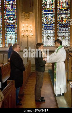 Katholische Männer stehen sich an, um vom römisch-katholischen Priester gesegnet zu werden, in einem jährlichen katholischen Ritual der Zeremonie zum Segen der Kehle am 3. Februar Kerzen werden an beiden Seiten der Kehle platziert. Die katholische Kirche St. Etheldreda. Ely Place London. HOMER SYKES AUS DEN 2000ER JAHREN Stockfoto