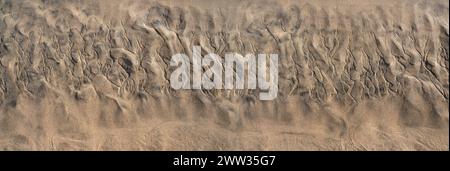 Abstrakte Struktur im braunen Sand am Strand bei Ebbe, unten mit flachem Wasser Stockfoto