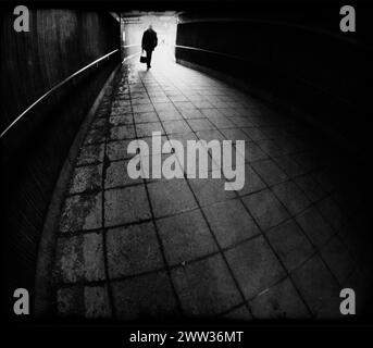 Silhouette eines Mannes, der in einen dunklen Tunnel eindringt, in Schwarz-weiß Stockfoto