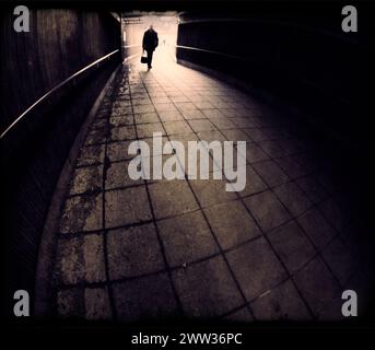 Silhouette eines Menschen, der in einen dunklen Tunnel eingeht, in Bronze monochrom Stockfoto