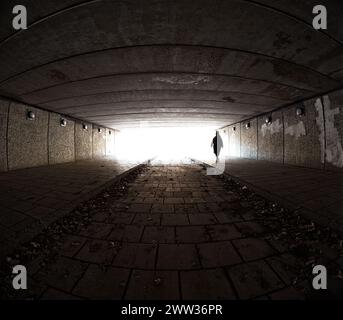 Dunkles Grungy-Bild einer Frau in verschwommener Bewegung, die durch einen städtischen Tunnel läuft. Stockfoto