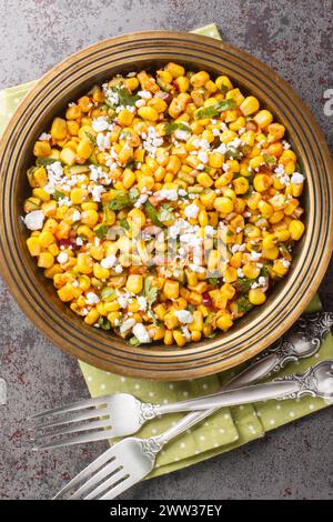 Esquites mexikanischer Street Corn Salat mit Jalapeno, Koriander, Cotija Käse, Zwiebeln und Gewürzen aus nächster Nähe auf dem Teller auf dem Tisch. Vertikale Draufsicht von Stockfoto