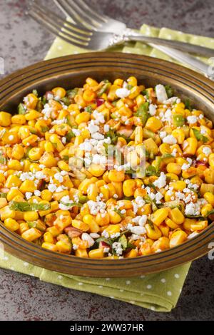 Esquites mexikanischer Street Corn Salat mit Jalapeno, Koriander, Cotija Käse, Zwiebeln und Gewürzen aus nächster Nähe auf dem Teller auf dem Tisch. Vertikal Stockfoto