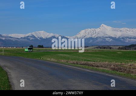 Bus auf der Straße mit Blick auf die schneebedeckten Berge (Blick auf Vysoke Tratry-krivan). Stockfoto