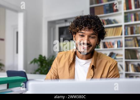 Ein glücklicher junger Mann arbeitet auf einem Laptop und lächelt in einem hellen Büro. Stockfoto