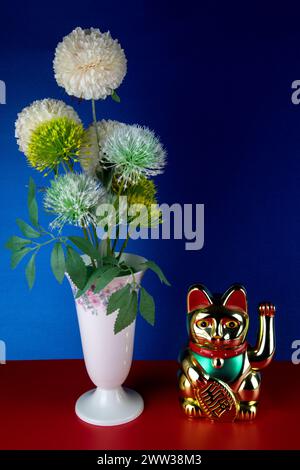 Porzellanvase mit künstlichen Blumen und goldfarbenem maneki-Neko, das Glückskatze hervorruft Stockfoto