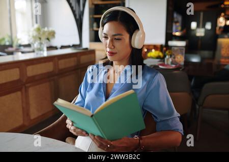 Frau sitzt am Restauranttisch und hört ruhige Musik in Kopfhörern und liest Planer Stockfoto