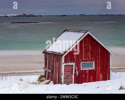 Rote rorbuer Fischerhütte am Strand im Schnee, Ramberg, Flakstadoya, Lofoten, Norwegen Stockfoto