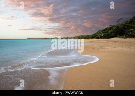 Einsamer, breiter Sandstrand mit türkisfarbenem Meer. Tropische Pflanzen in einer Bucht bei Sonnenuntergang in der Karibik. Plage de Cluny, Basse Terre, Guadeloupe Stockfoto