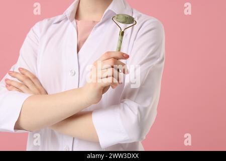 Kosmetologe mit Gesichtsrolle auf rosa Hintergrund, Nahaufnahme Stockfoto