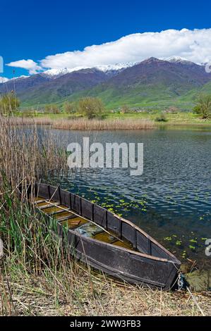 Blick auf Kerkini See im Norden Griechenlands ist mit traditionellen Holzmöbeln Fischerboot und Teil des schneebedeckten Mount Beles Stockfoto