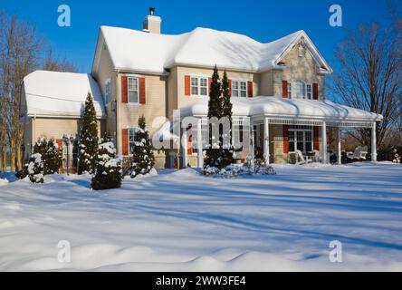 Zweistöckiges beigefarbenes Vinyl-Nebengebäude mit bräunlich-roten Ziegel-Furnier und orangefarbenen Zierleisten im Winter in Quebec, Kanada Stockfoto